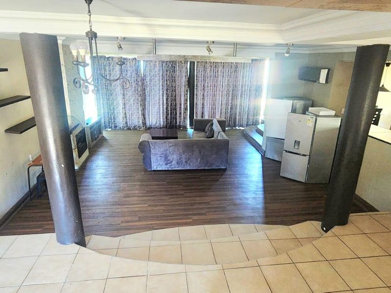 Spacious open-plan living area featuring a split-level design, structural columns, laminate and tiled flooring, and direct access to the outdoors via sliding doors.