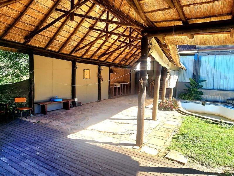Spacious covered patio featuring a traditional thatched roof, timber decking, and a built-in outdoor counter, overlooking a private swimming pool and garden area.