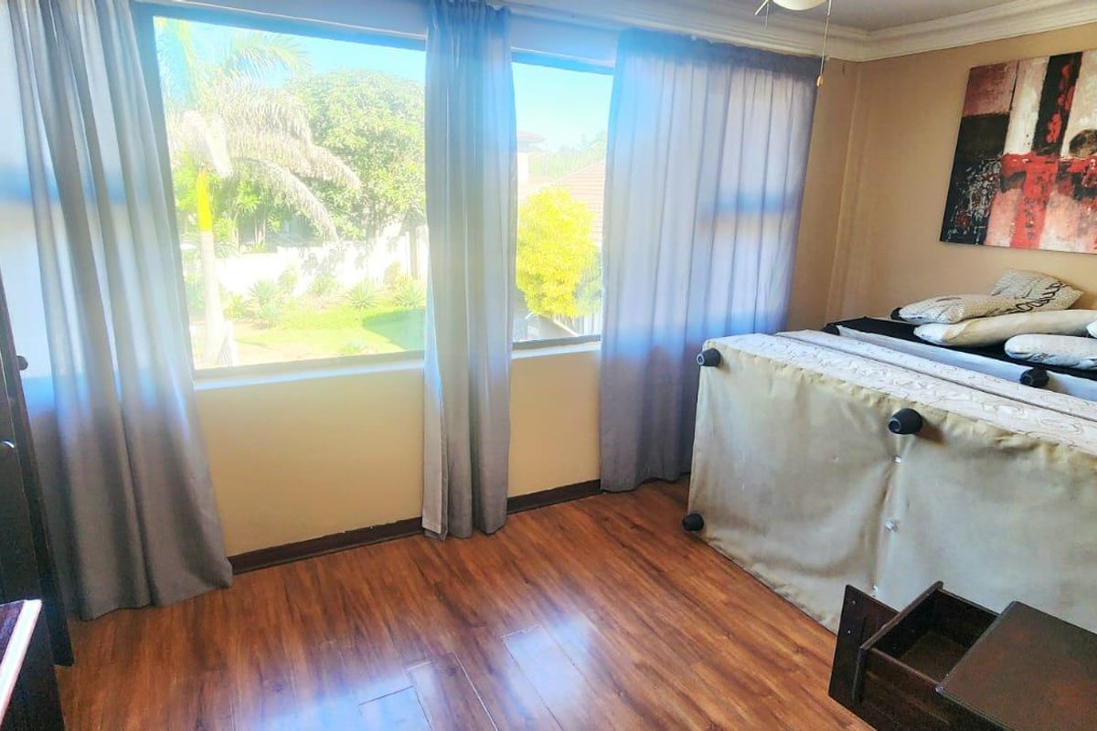 A bedroom featuring laminate flooring and large windows that provide natural light and garden views.