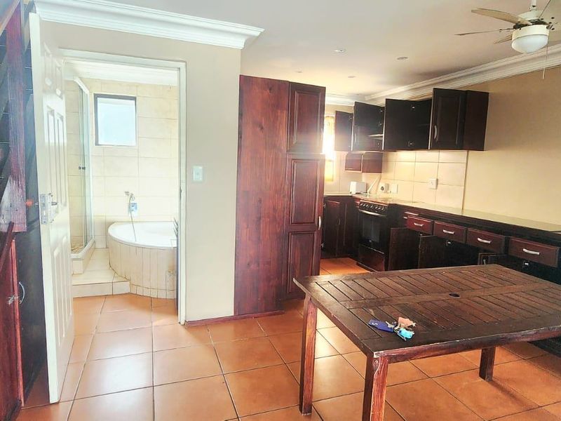 Open plan kitchen and living area featuring dark wood cabinetry, tiled flooring, and an adjoining bathroom with a bathtub and shower.