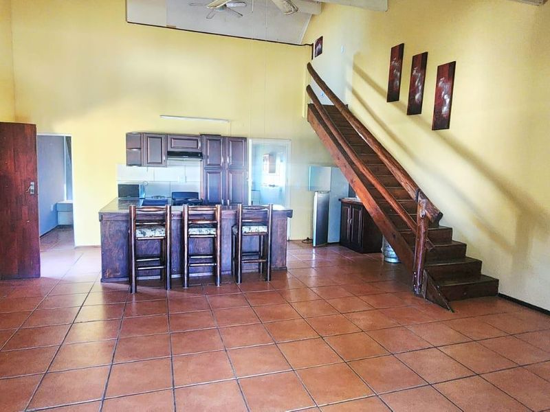 Open-plan living area featuring a kitchen with built-in cabinetry, a central island, and a wooden staircase leading to an upper level.
