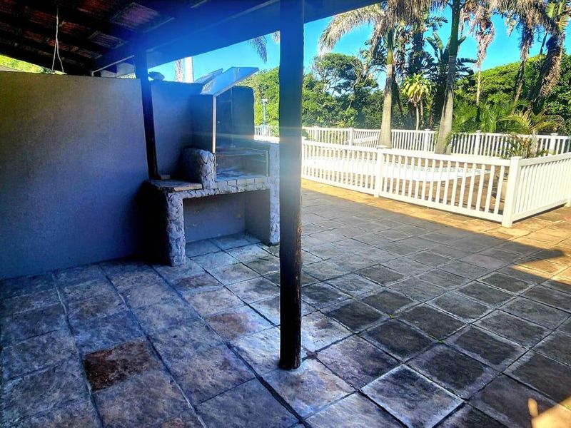 Covered outdoor patio featuring a built-in braai, paved flooring, and direct access to the pool area and garden.