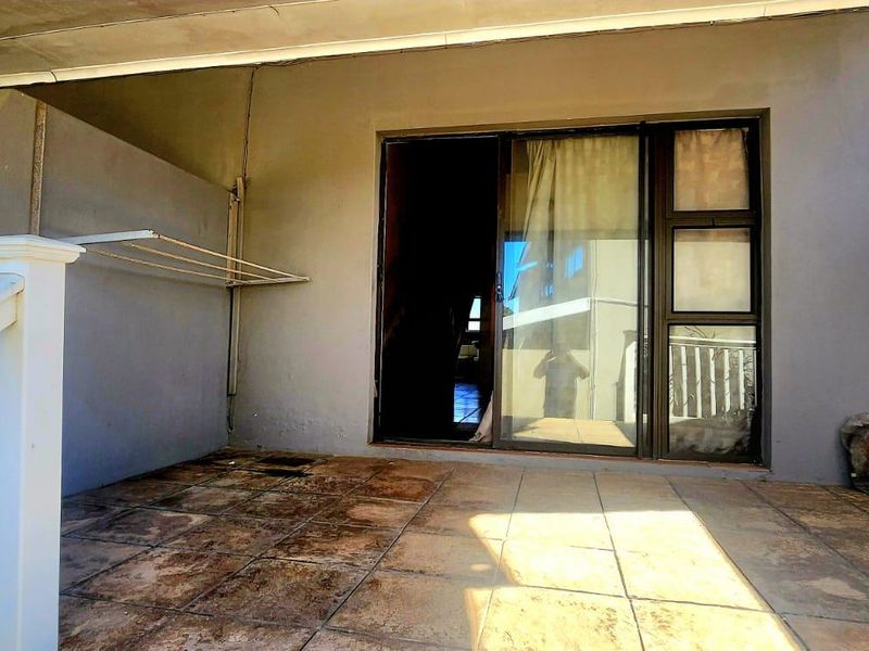 A covered patio area featuring tiled flooring, a sliding glass door entrance, and a wall-mounted drying rack, requiring some maintenance and cosmetic updates.