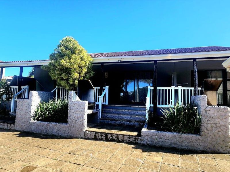Rear exterior view featuring a covered patio, stone-clad retaining walls, and a paved terrace area suitable for outdoor entertaining.