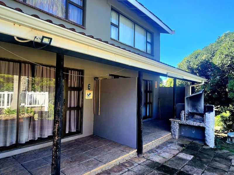A covered patio area featuring a built-in braai, tiled flooring, and direct access to the home via sliding doors, overlooking the garden.