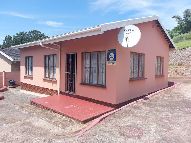 Front exterior view of a single-story house featuring a painted facade, brick base, security gate, and concrete patio area.