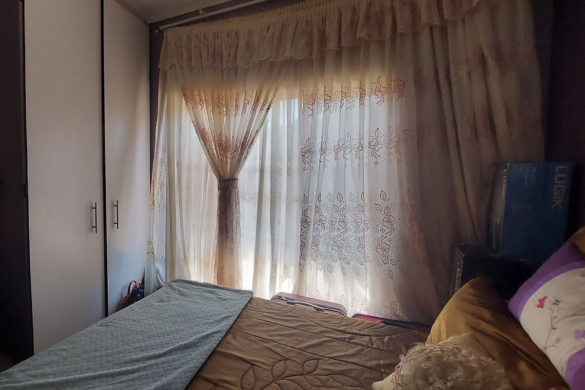 A bedroom featuring built-in cupboards and large window with curtains, providing natural light.