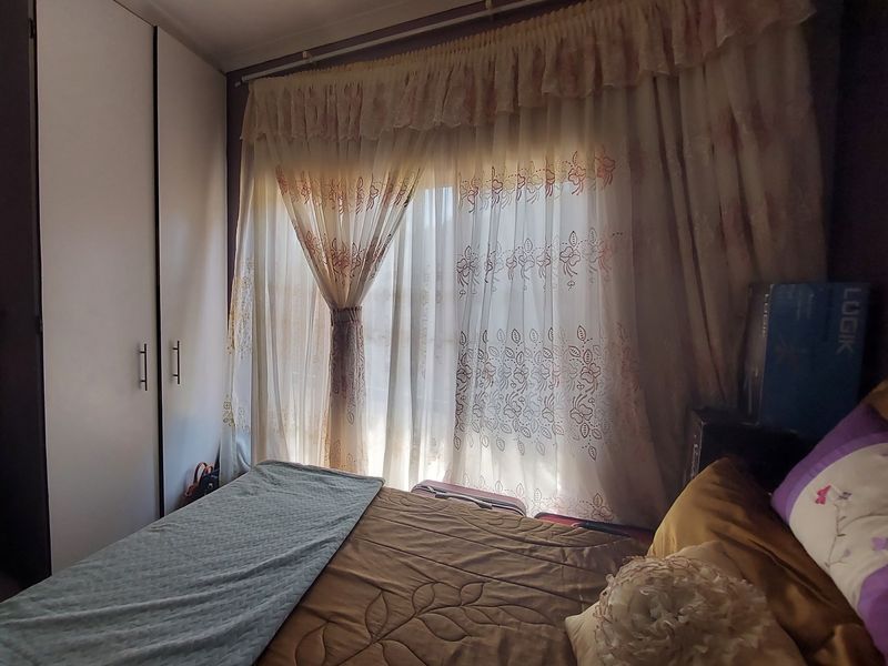 A bedroom featuring built-in cupboards and large window with curtains, providing natural light.