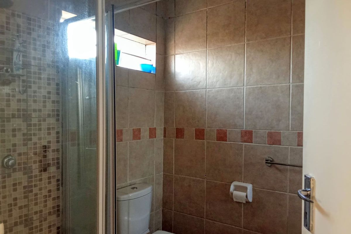 A functional bathroom featuring a shower enclosure with mosaic tiling, a standard toilet, and neutral ceramic wall tiles.