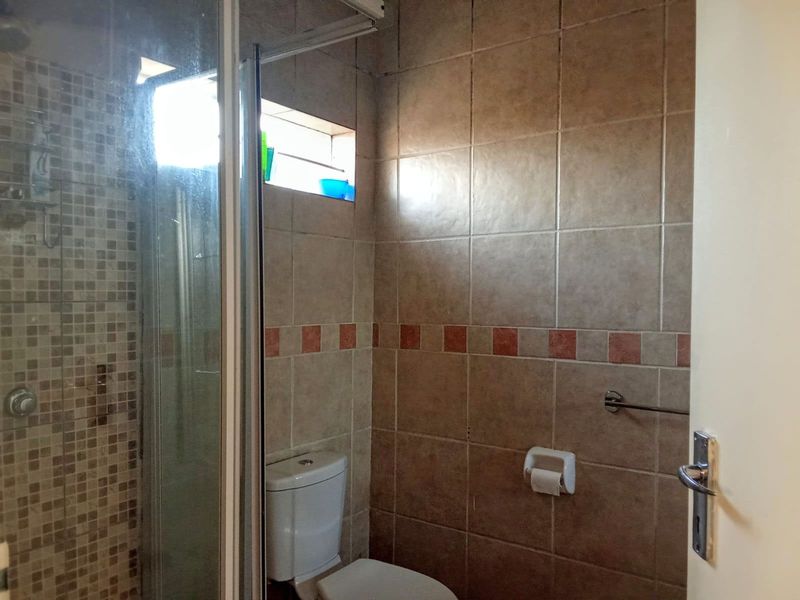 A functional bathroom featuring a shower enclosure with mosaic tiling, a standard toilet, and neutral ceramic wall tiles.