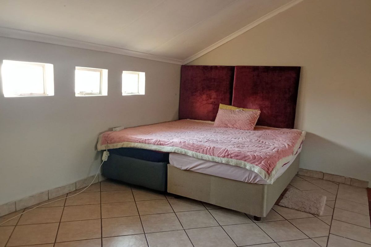 A bedroom featuring tiled flooring and a sloped ceiling with three small windows, providing a cozy attic-style living space.