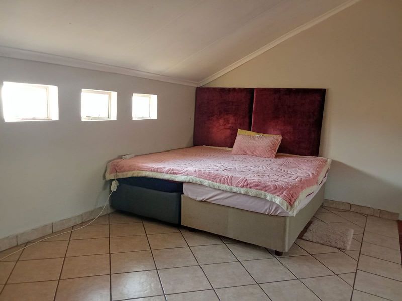 A bedroom featuring tiled flooring and a sloped ceiling with three small windows, providing a cozy attic-style living space.