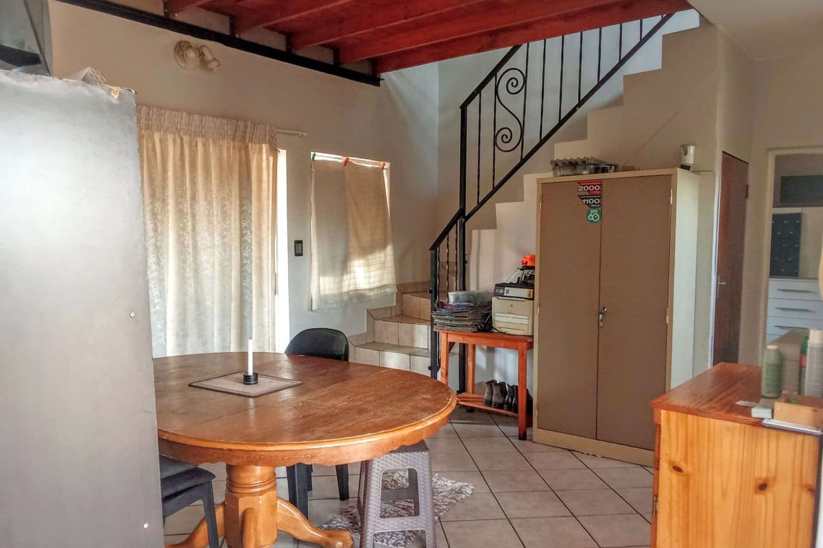 Living area featuring exposed timber ceiling beams, tiled flooring, and a wrought iron staircase leading to the upper level.