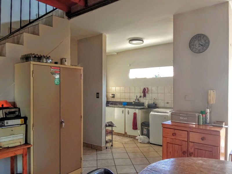 A functional kitchen area featuring tiled flooring, built-in cabinetry, and a tiled backsplash, situated adjacent to an internal staircase.