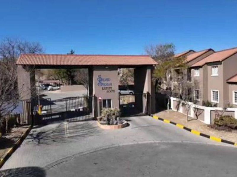 Entrance view of the residential estate featuring a secure gated access point, guard house, and paved driveway leading into the complex.