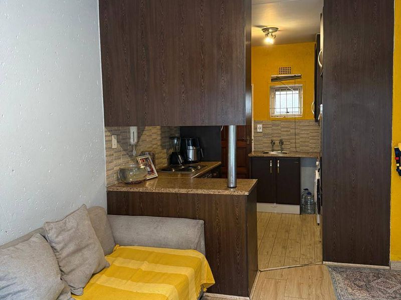 Open-plan living area featuring a compact kitchen with dark wood cabinetry, stone-look countertops, and light wood-look flooring, seamlessly connected to the adjacent living space.