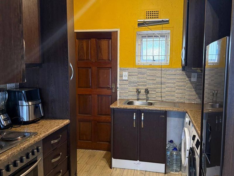 A functional kitchen featuring dark wood cabinetry, granite-look countertops, a built-in oven with hob, and integrated laundry appliance connections.