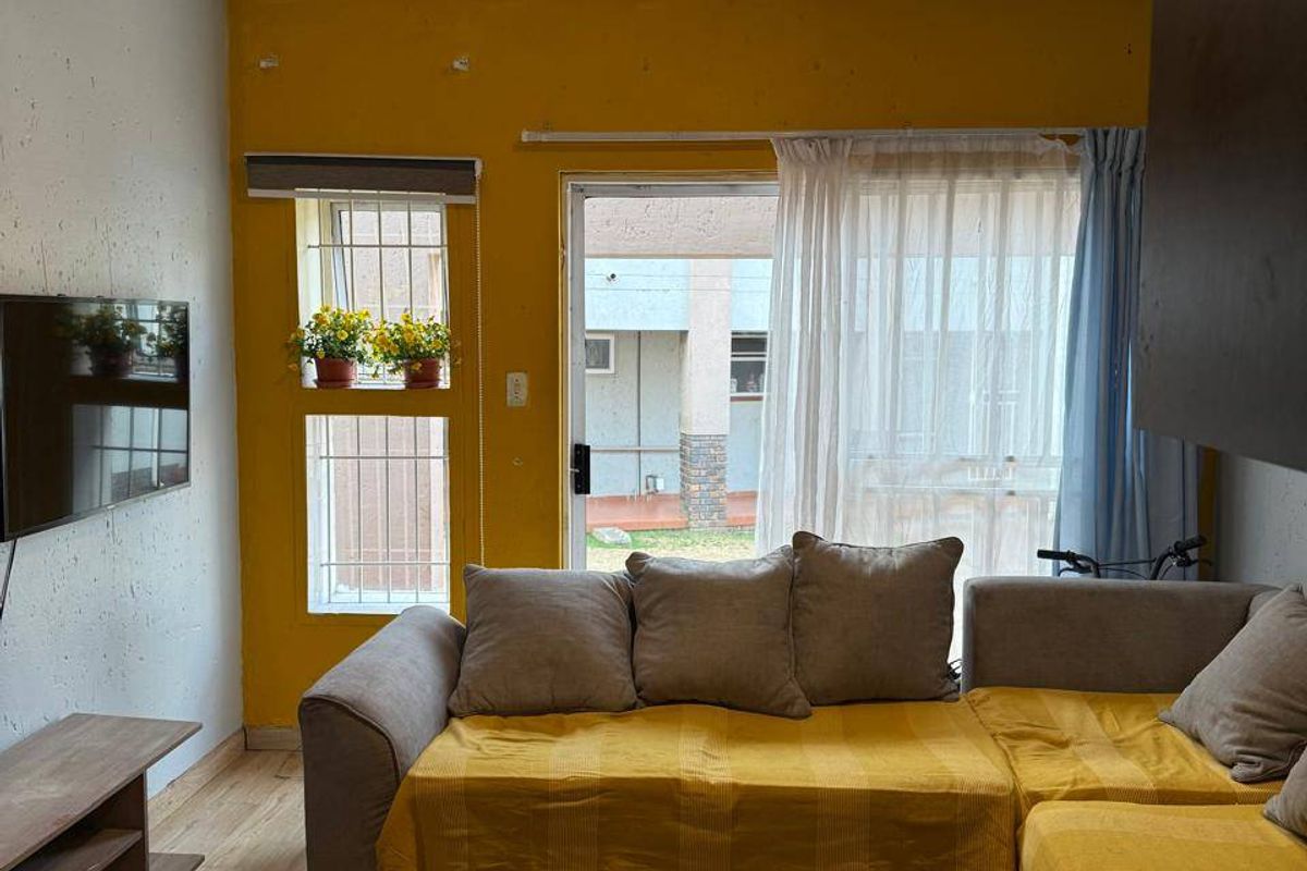 A living room featuring laminate flooring, a yellow accent wall, and a glass door providing access to the exterior patio area.