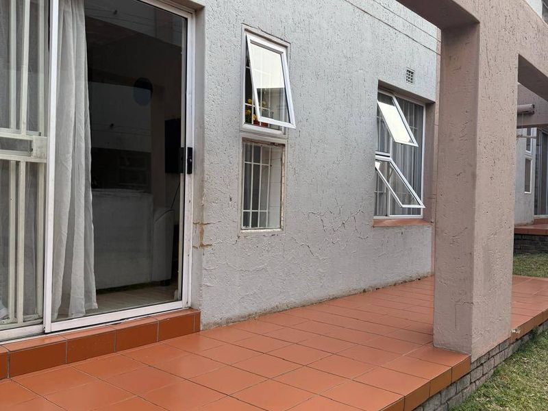 A covered patio area with tiled flooring, featuring sliding glass doors and top-hung windows leading into the townhouse interior.