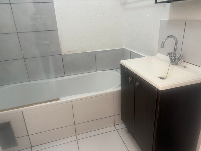 A functional bathroom featuring a bathtub with a glass screen, a vanity cabinet with a basin, and tiled finishes.
