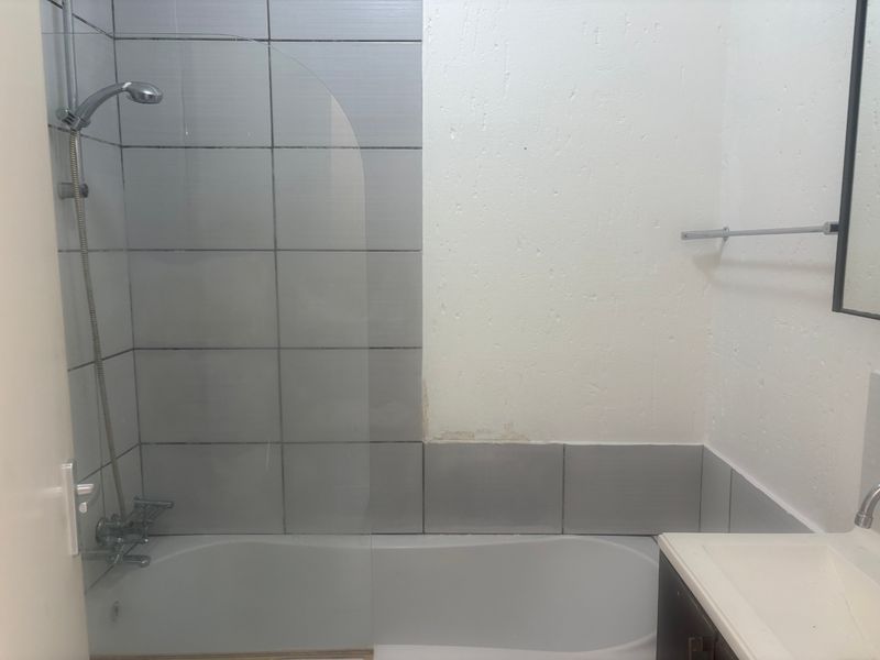 A functional bathroom featuring a bathtub with a glass shower screen, tiled splashback, and a vanity unit, requiring some cosmetic wall repairs.