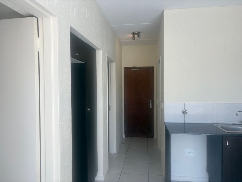 A functional hallway area featuring tiled flooring, built-in cabinetry, and a compact kitchen sink station with a dark countertop.