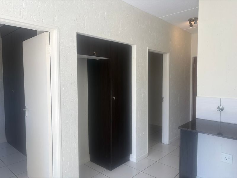 A clean, empty hallway featuring tiled flooring, built-in dark wood cabinetry, and a small granite counter area, providing functional transition space within the apartment.