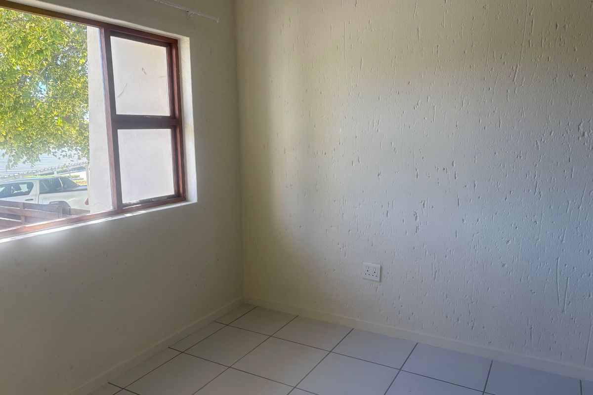An empty bedroom featuring white tiled flooring, textured walls, and a timber-framed window providing natural light.