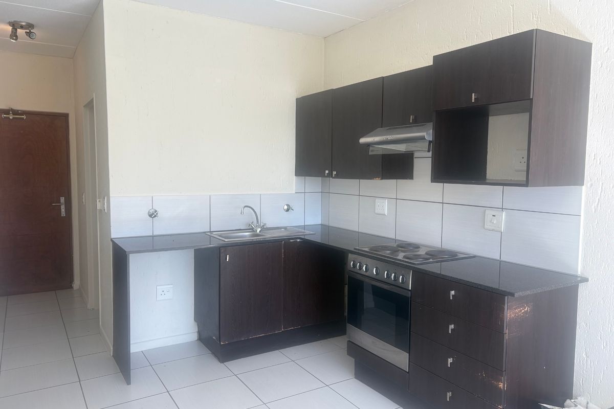 A functional kitchen featuring dark wood cabinetry, granite countertops, built-in oven, hob, and extractor fan, with tiled flooring and backsplash.