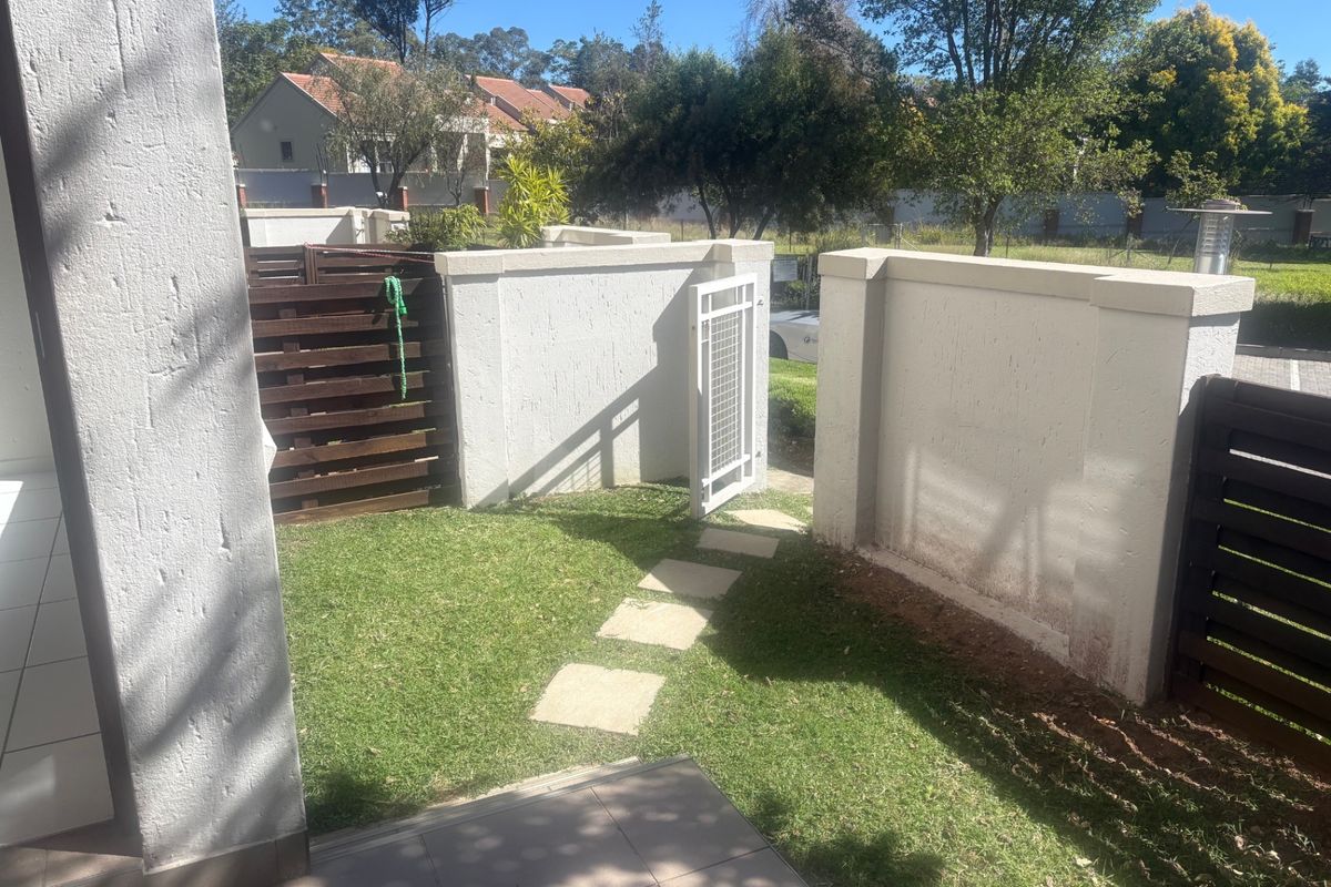 A private rear garden area featuring a paved path, lawn, timber privacy screening, and a secure pedestrian gate set within a boundary wall.