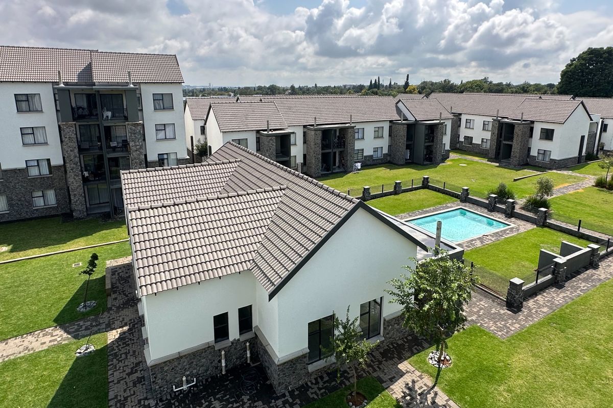 Aerial view of a modern apartment complex featuring well-maintained lawns, paved pathways, and a communal swimming pool area.