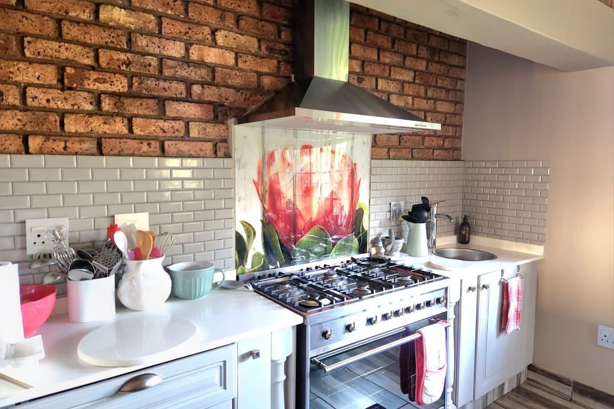 A well-appointed kitchen featuring a striking exposed brick wall, subway tile backsplash, custom floral glass splashback, and a professional-grade stainless steel gas stove.