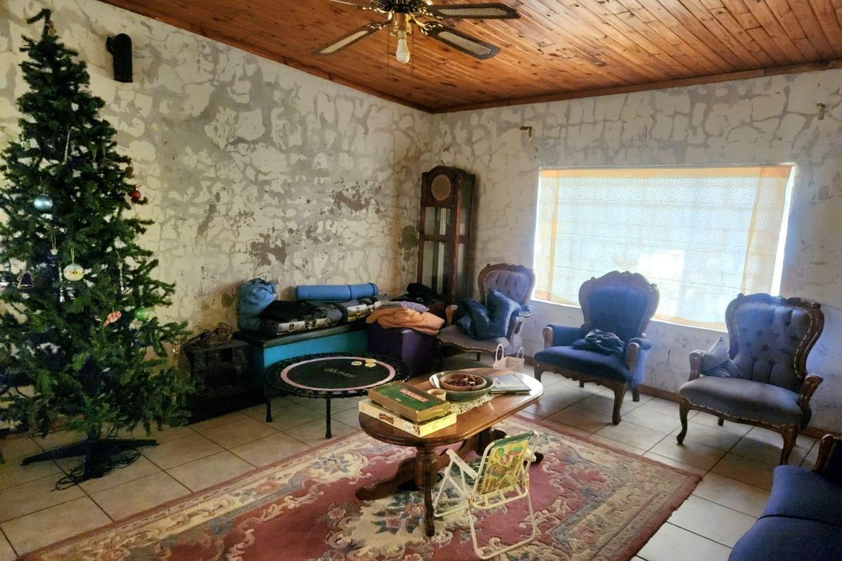 A living room featuring a timber ceiling, ceiling fan, and tiled flooring, currently requiring significant wall repairs and cosmetic updates.