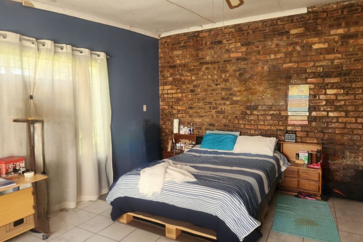 A bedroom featuring an exposed brick feature wall, tiled flooring, and a ceiling fan, requiring some maintenance to the ceiling finishes.