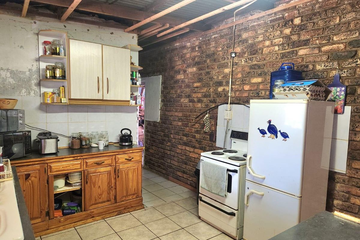 A rustic kitchen featuring exposed brick walls, timber cabinetry, and exposed ceiling rafters, offering significant potential for renovation and modernization.