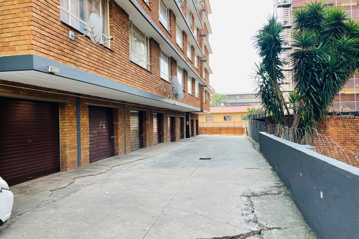 Exterior view of an apartment complex featuring a row of ground-level garages and a concrete driveway with perimeter security fencing.