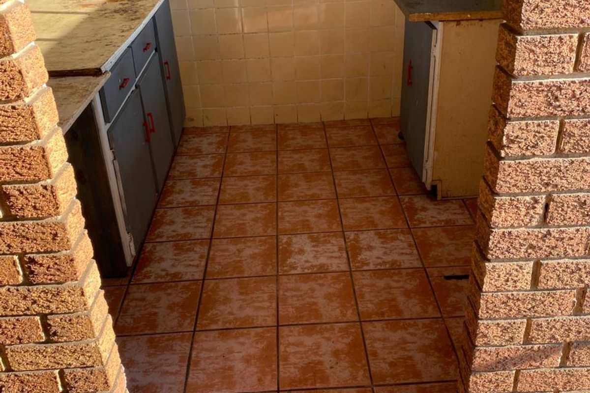 A dated kitchen area featuring exposed brick pillars, tiled flooring, and original cabinetry, offering significant potential for a modern renovation.