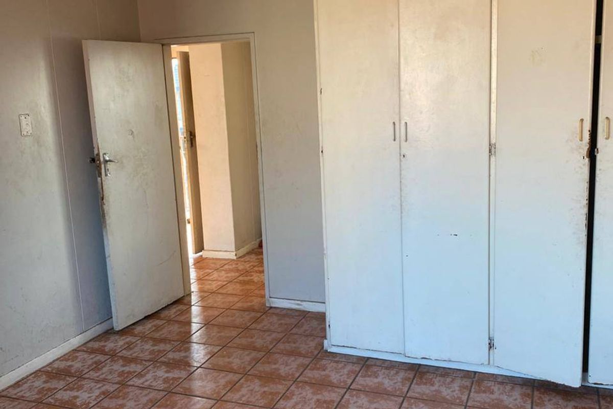 A vacant bedroom featuring tiled flooring and built-in storage cupboards, requiring cosmetic updates and maintenance to restore its appeal.