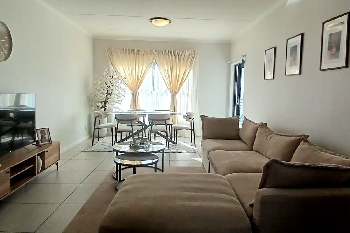 An open-plan living and dining area featuring neutral tiled flooring, ample natural light, and direct access to an outdoor space through a sliding glass door.