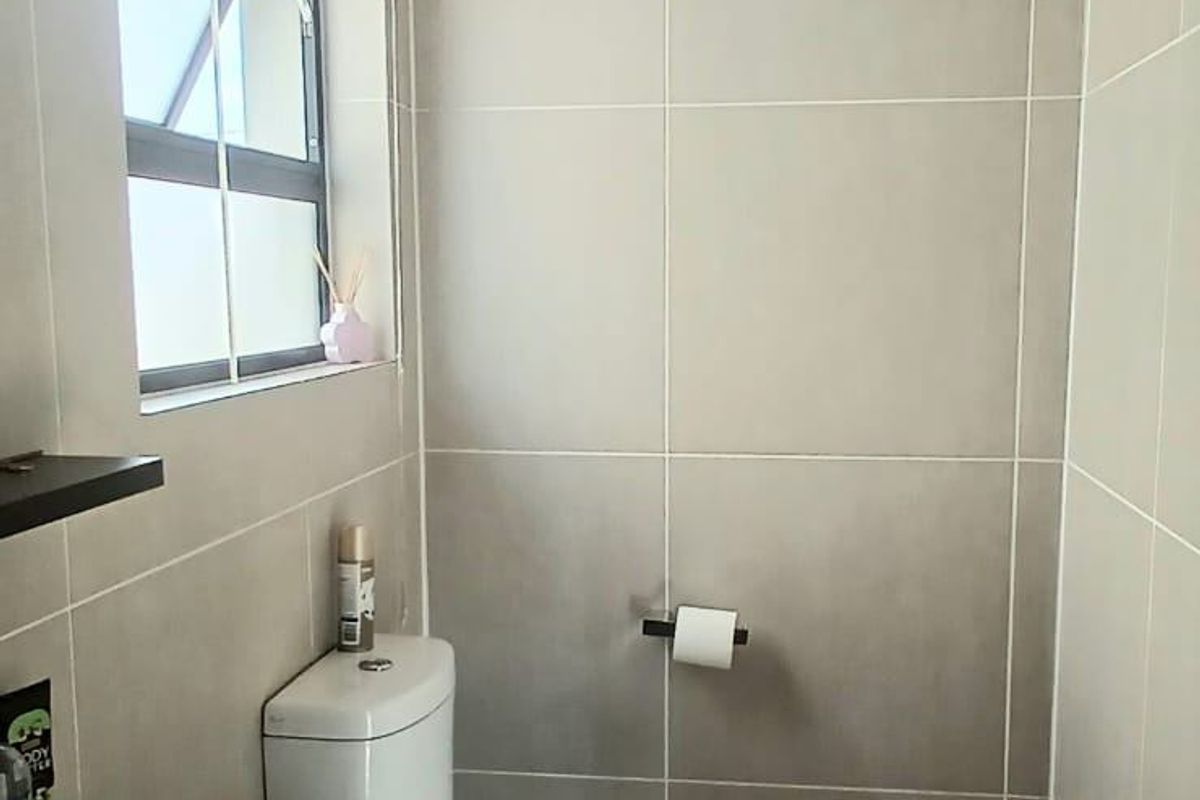 A modern, compact bathroom featuring neutral floor-to-ceiling wall tiles, a sleek vanity cabinet with a basin, and a functional toilet.