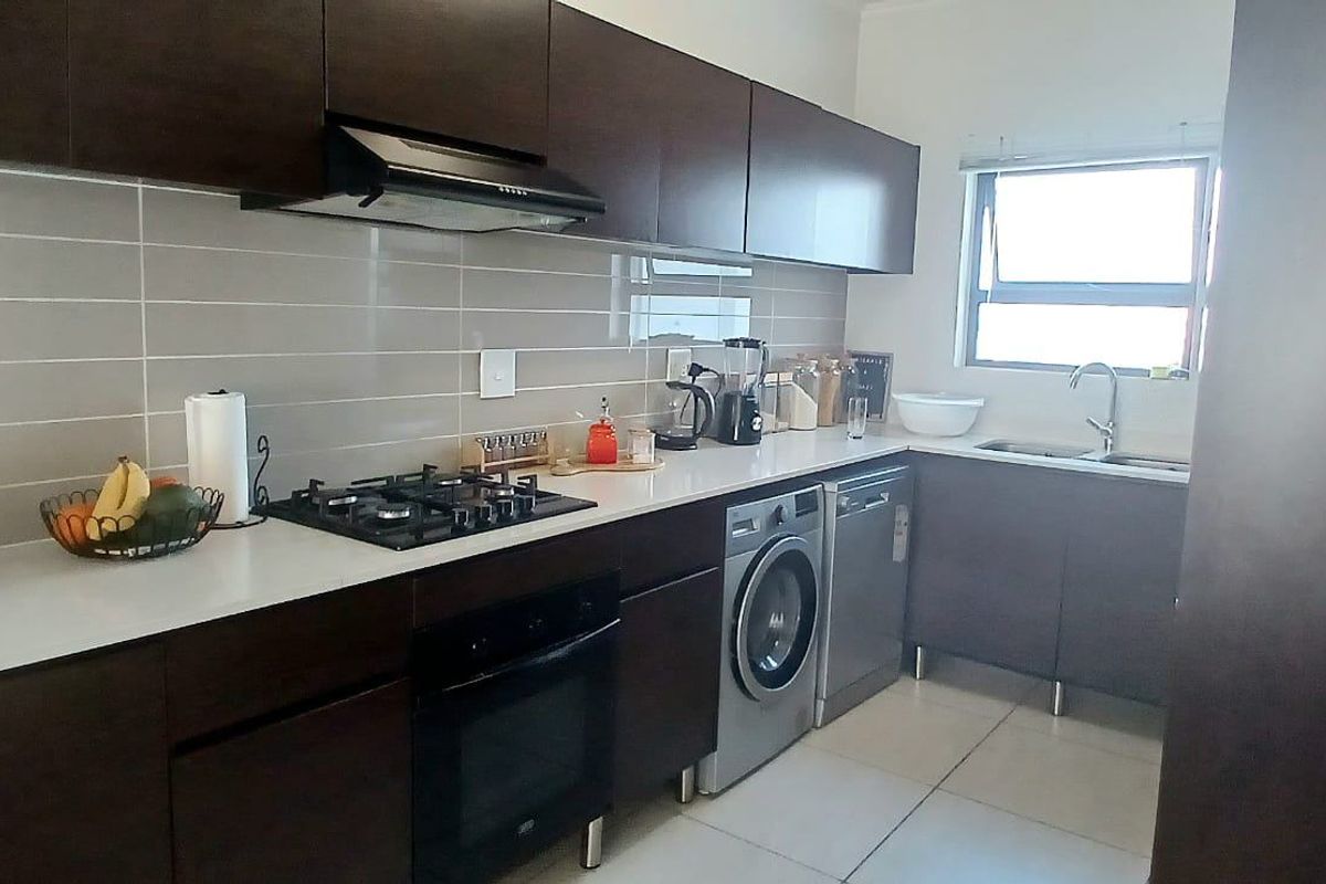 Modern kitchen featuring dark wood cabinetry, stone countertops, gas hob, built-in oven, and integrated laundry appliance space.