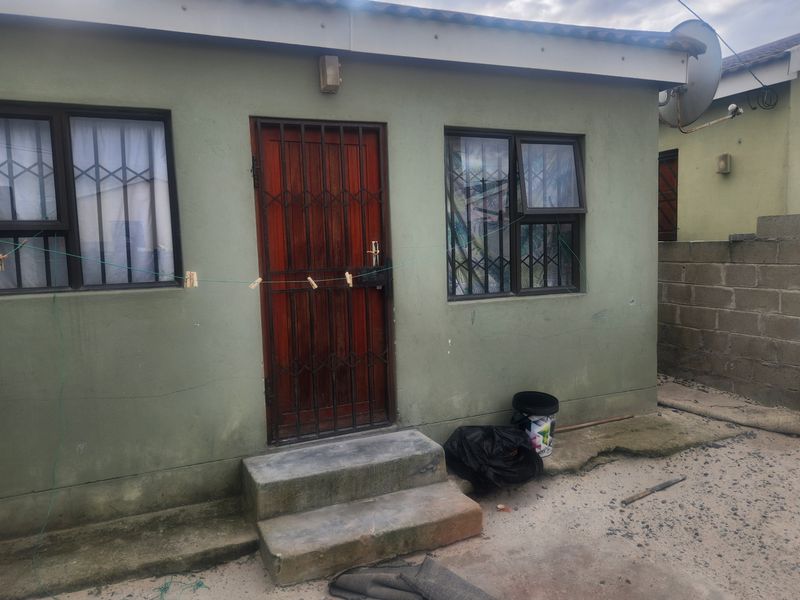 Rear exterior view of the property featuring a security gate, concrete steps, and aluminium window frames with a concrete block boundary wall.