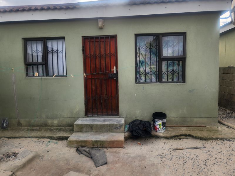 Rear exterior view of a single-story house featuring a security gate, concrete steps, and aluminium window frames.