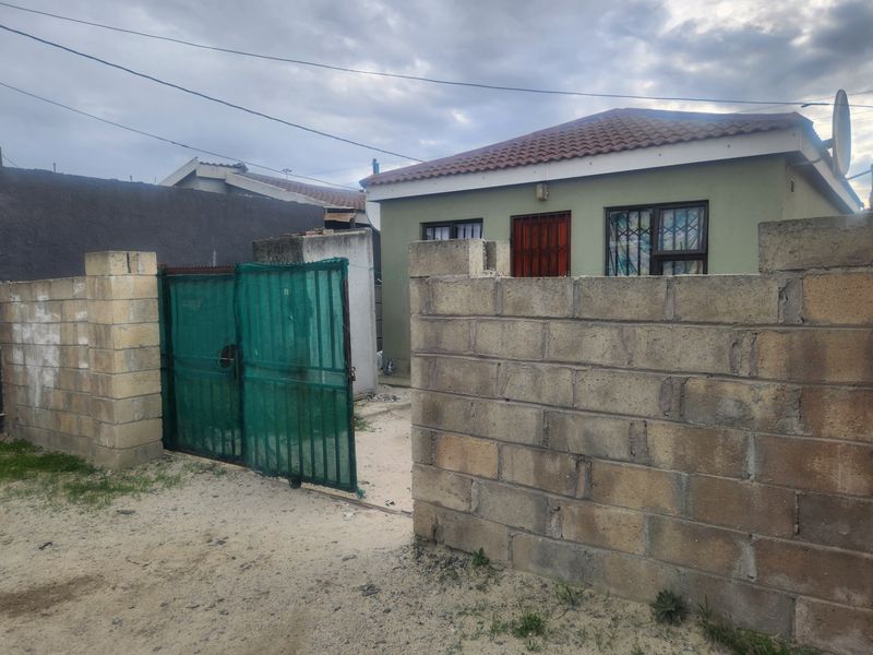 Front view of a detached house featuring a concrete block boundary wall, metal security gate, and tiled roof with security bars on windows.