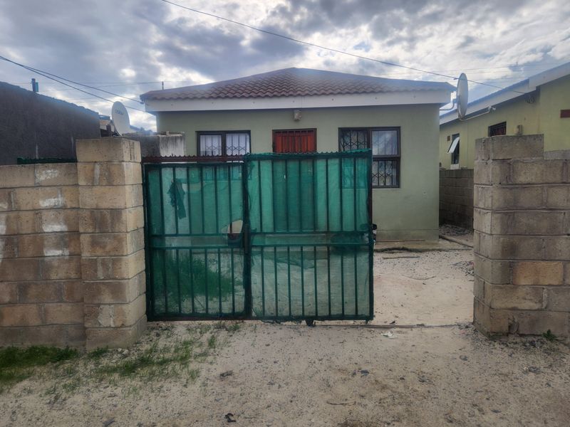 Front view of a single-story house featuring a concrete block boundary wall, metal security gate, and tiled roof.