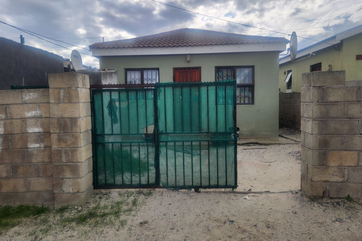 Front view of a single-story house featuring a concrete block boundary wall, metal security gate, and tiled roof.