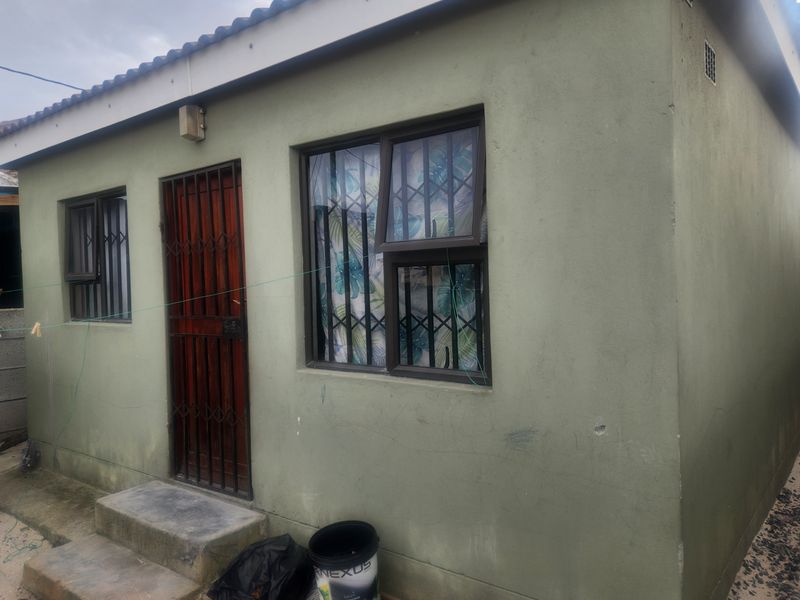 Exterior view of the rear facade featuring a security gate, aluminium window frames with security bars, and concrete steps leading to the entrance.
