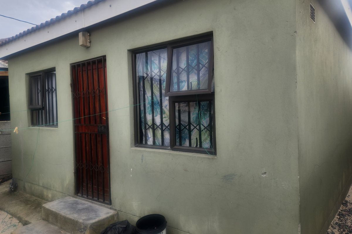 Exterior view of the rear facade featuring a security gate, aluminium window frames with security bars, and concrete steps leading to the entrance.