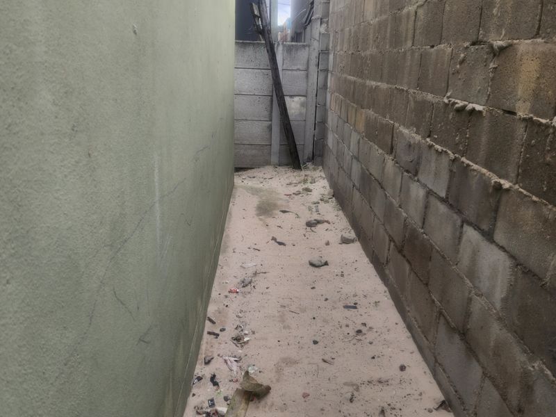 A narrow side passage between the house and the boundary wall, featuring unfinished masonry and requiring landscaping and cleanup.