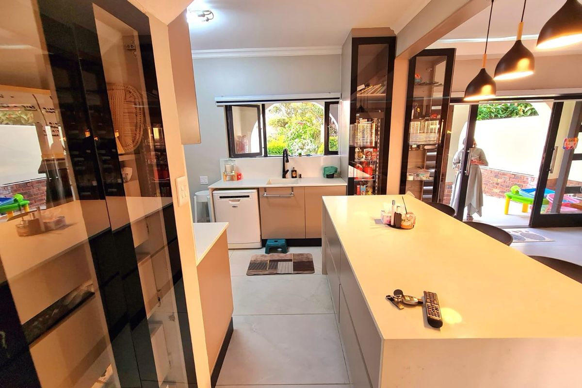Modern kitchen featuring a large central island, sleek cabinetry, integrated dishwasher, and glass display units, with direct access to an outdoor patio area.